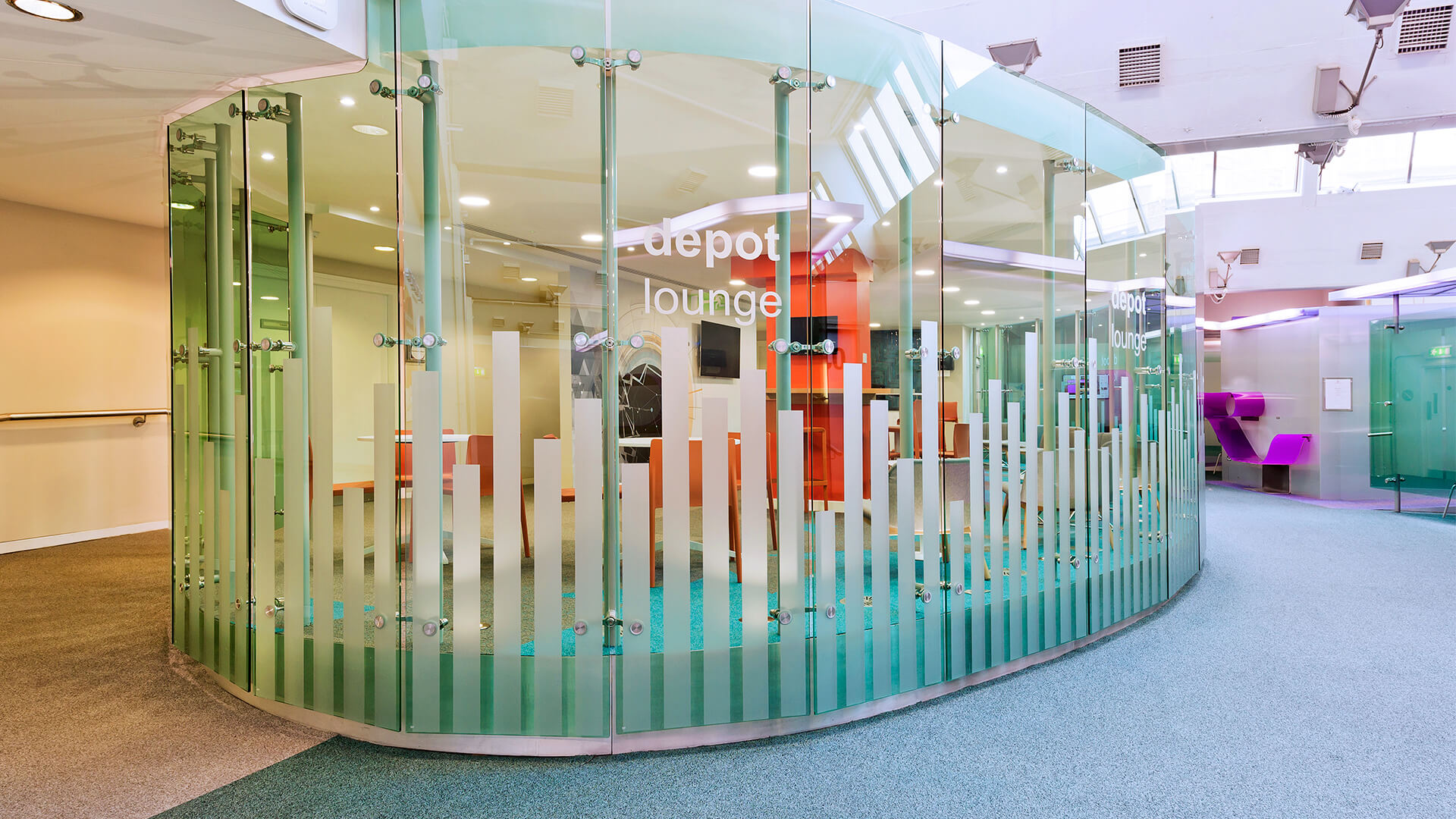 A curved glass wall with a decal reading "depot lounge" frames a bright seating area