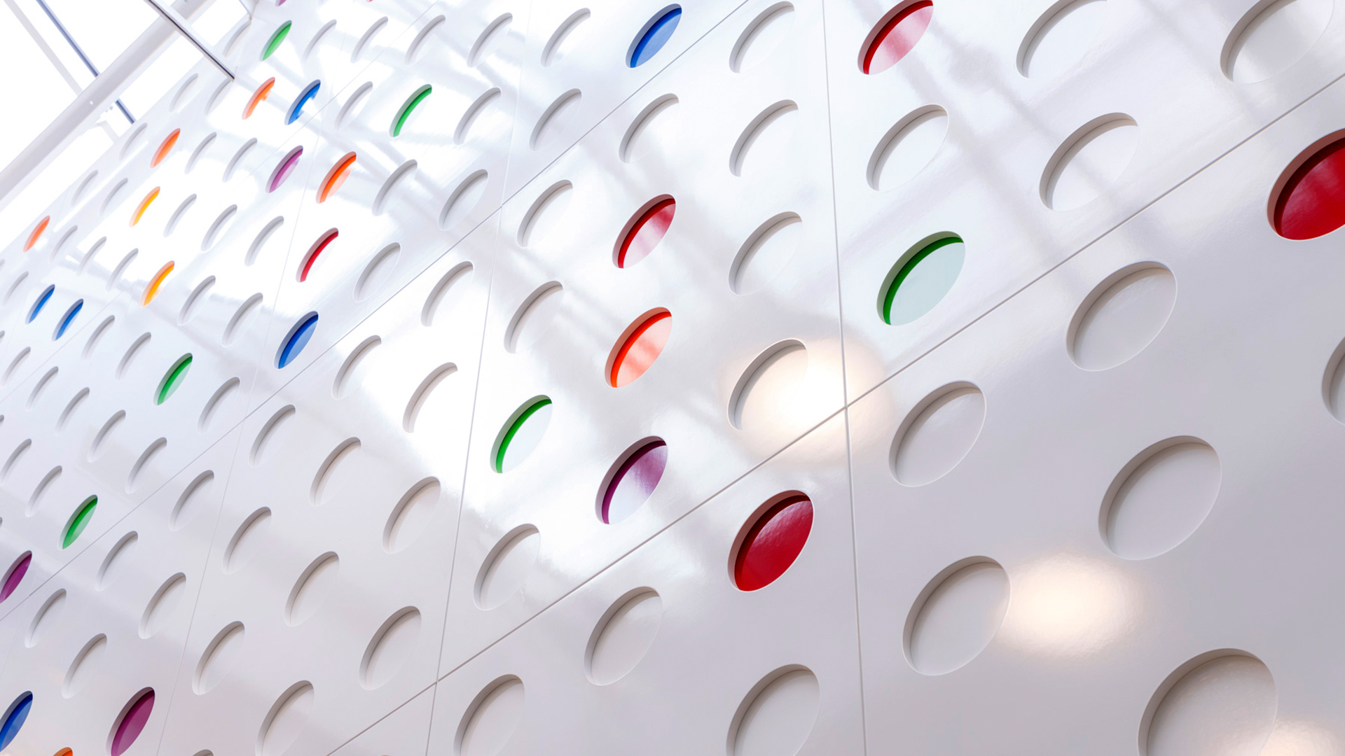 A detail of the Gainstore Atrium wall, which displays a series of white recessed circles, some filled with bright colours