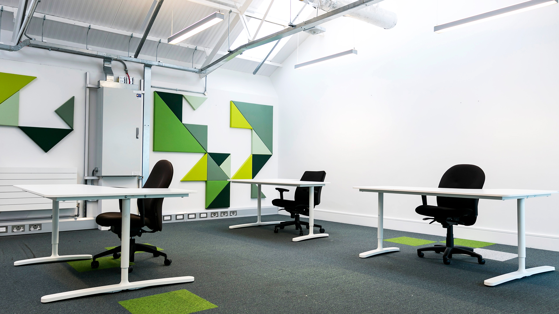 A bright and light office space with desks and green geometric murals on the white walls