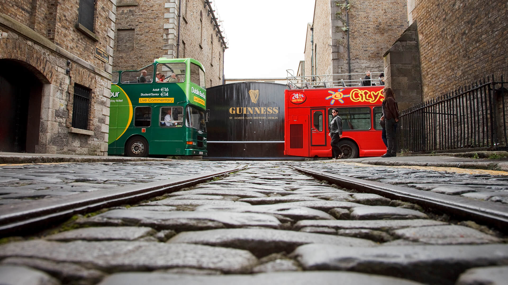 Green and red Dublin tourism buses stand in front of St. James's Gate at the Guinness Brewery