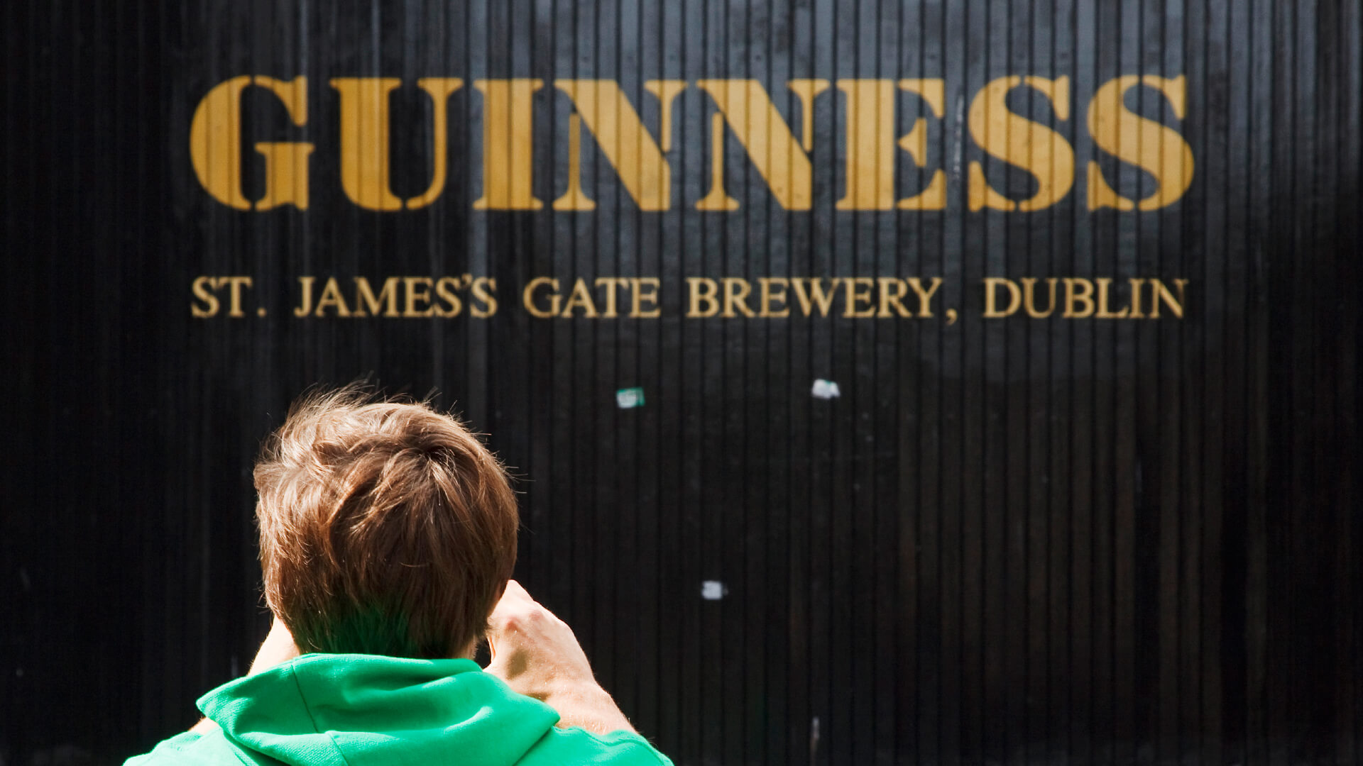 A man takes a photo of St James's Gate. On it, painted in gold, are the words: "Guinness St. James's Gate Brewery, Dublin"